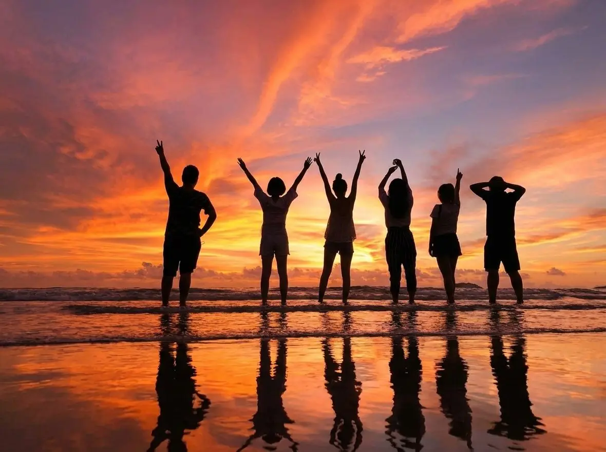 Silhouettes of a group with their arms raised on a beach at sunset