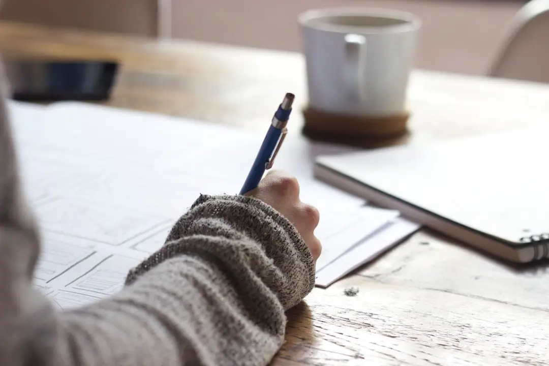 Close-up of a hand filling in a form beside a cup of coffee