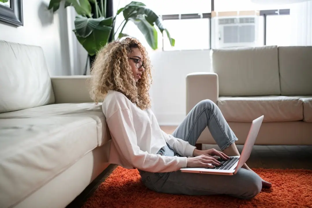 A person sitting on the floor against a sofa, using a laptop