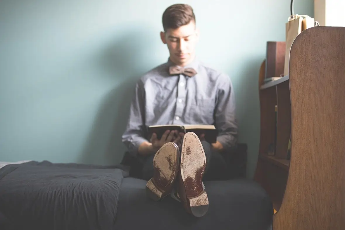 A person sitting on a bed reading a book in a quiet, dim room