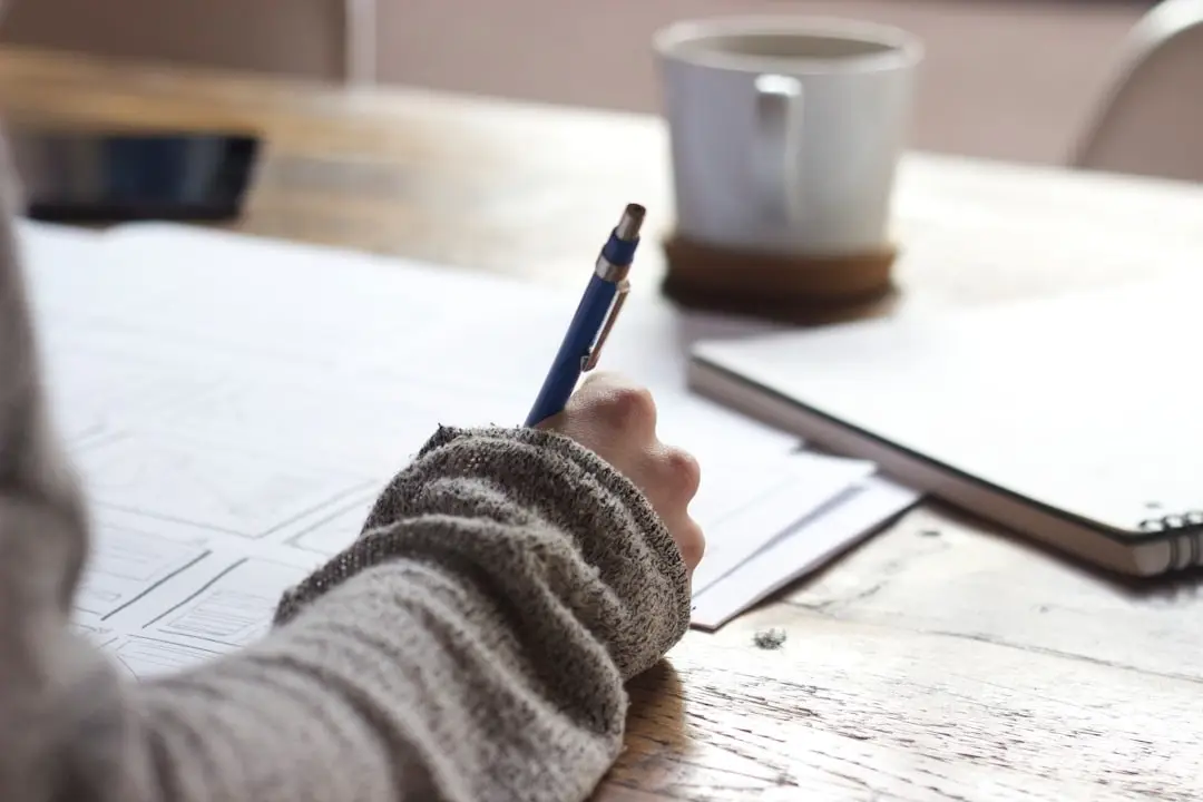 Close-up of a hand filling in a form beside a mug