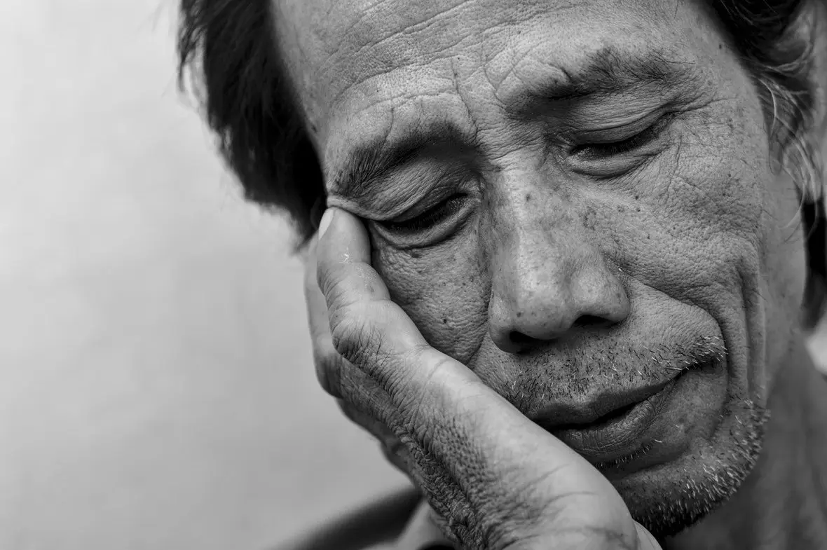 A black and white portrait of an older person resting their head on their hand