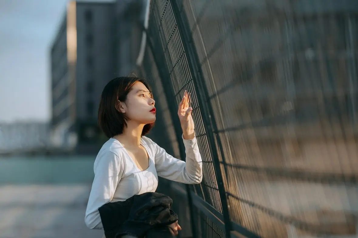 A person standing with a hand against a fence beside the water