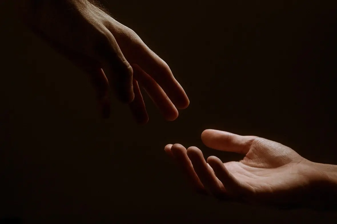 Two hands reaching toward one another in low light