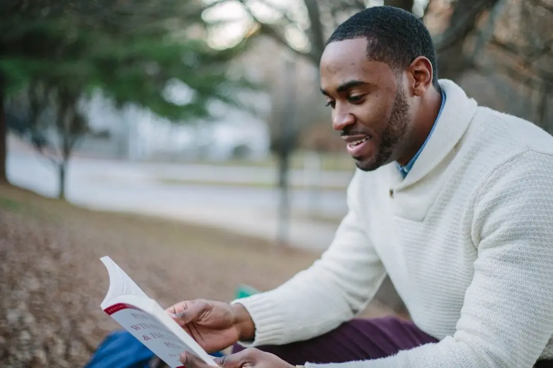 A person reading a book outdoors on a bench
