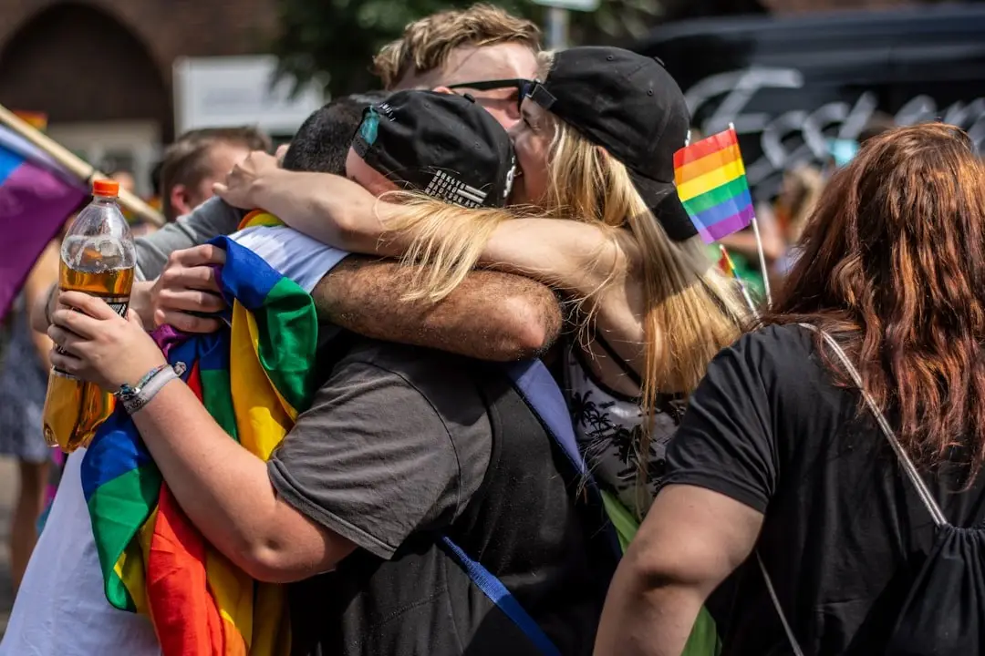 Friends hugging at a Pride event, rainbow flags around them