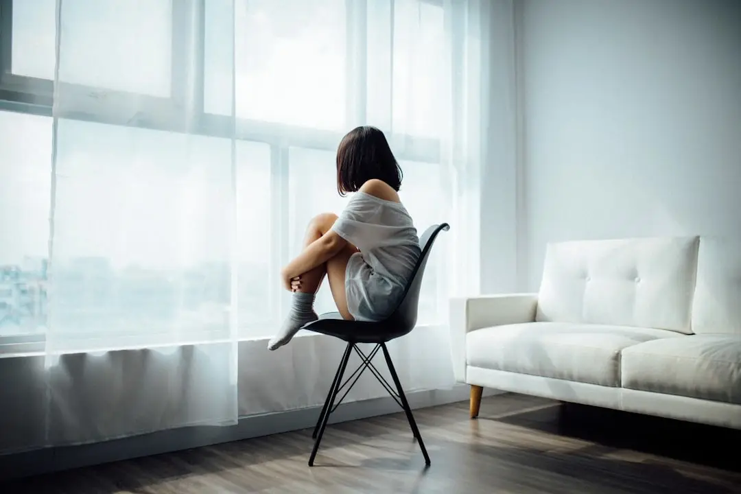 A person sitting alone on a chair beside a bright window