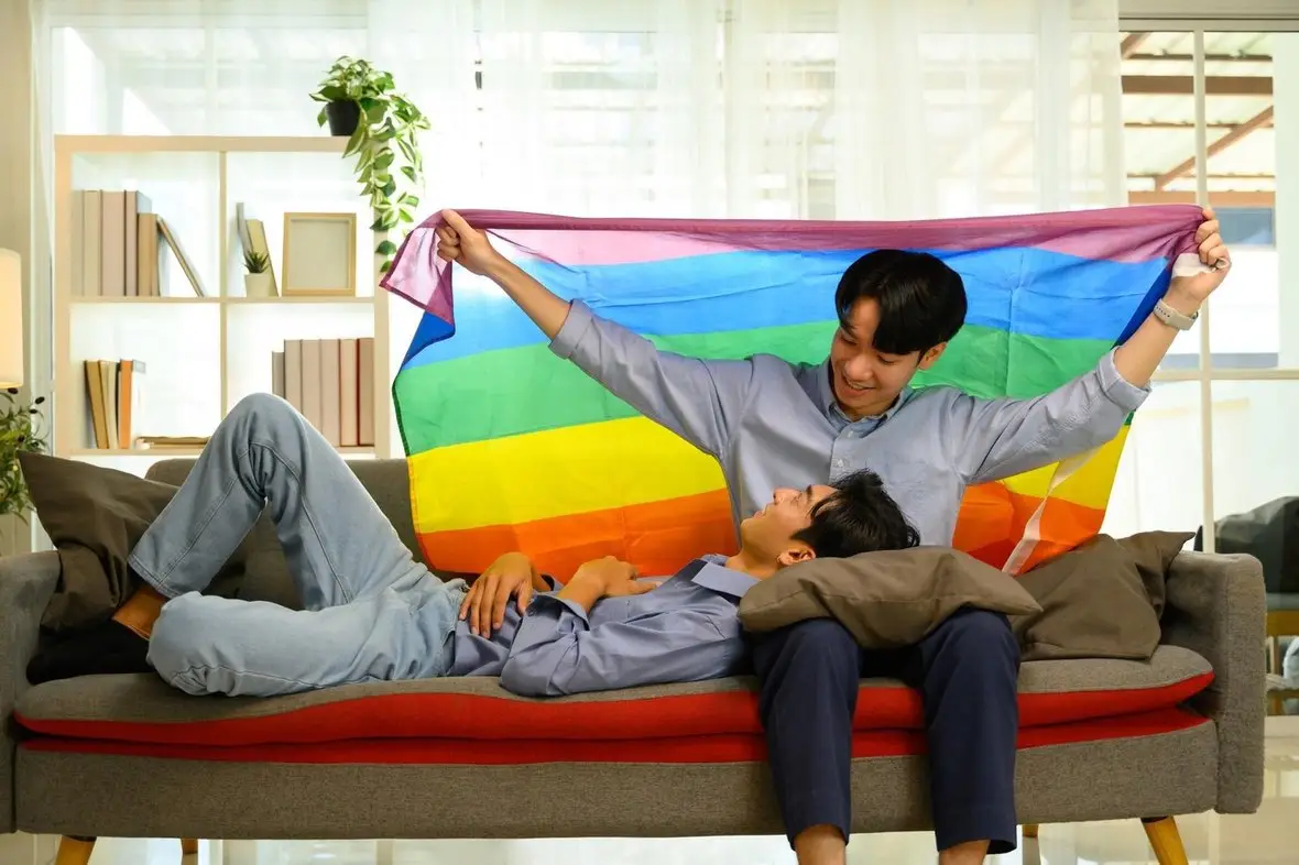 Two people holding up a rainbow flag together on a sofa